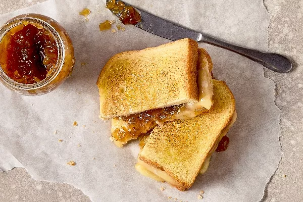 A top view of an Onion Jam Grilled Cheese Sandwich cut in half, placed on parchment paper. The golden-brown toasted sandwich reveals melted cheese and caramelized onion jam.