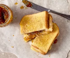 A top view of an Onion Jam Grilled Cheese Sandwich cut in half, placed on parchment paper. The golden-brown toasted sandwich reveals melted cheese and caramelized onion jam.