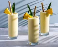 Three glasses of Piña Colada garnished with pineapple spears and leaves, with bamboo straw